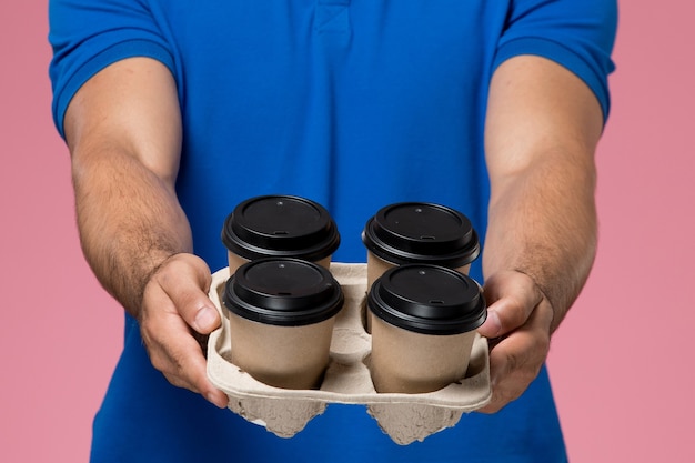 Corriere maschio di vista ravvicinata anteriore in uniforme blu che consegna tazze di caffè sul rosa, consegna di servizio uniforme del lavoratore
