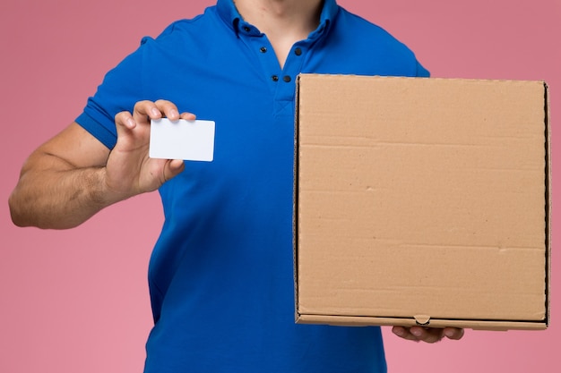 Front close view male courier in blue uniform holding white card food box on pink, worker uniform service delivery