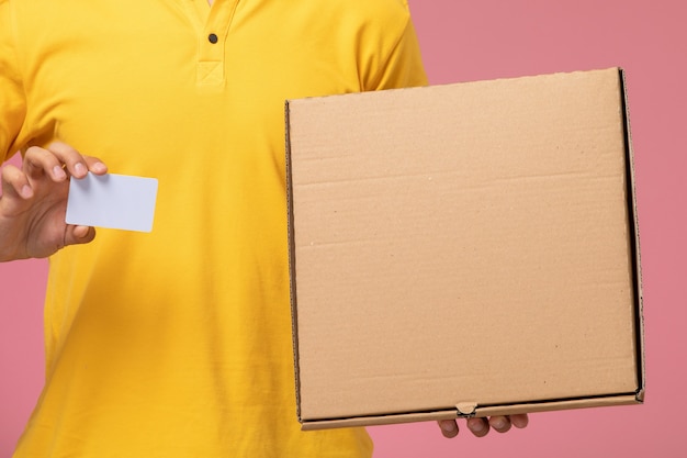 Free photo front close view male courier in yellow uniform holding grey card and food delivery box on the pink desk