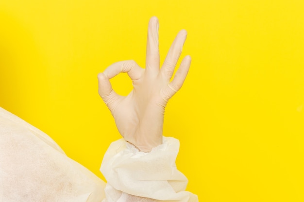 Front close view of male scientific worker in special protective suit and showing alright sign on yellow wall