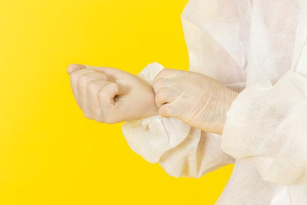 Front close view of male scientific worker in special protective suit and with mask wearing gloves on yellow wall