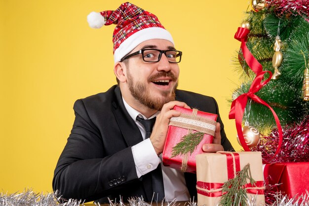 front close view male worker sitting around presents and little tree on a yellow 
