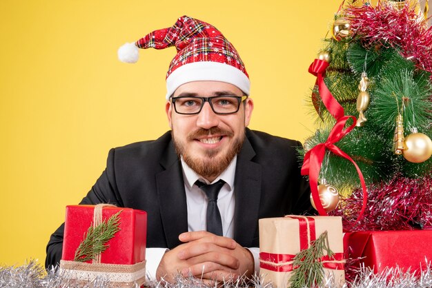 front close view male worker sitting around presents and little tree on yellow 