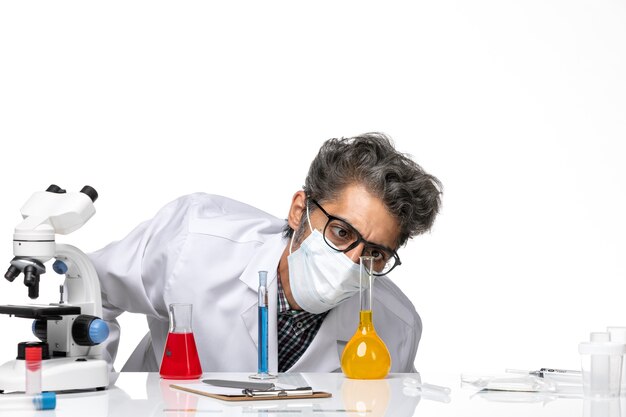 Front close view middle-aged scientist in special suit sitting with solutions checking them on a white background male virus science covid- chemistry