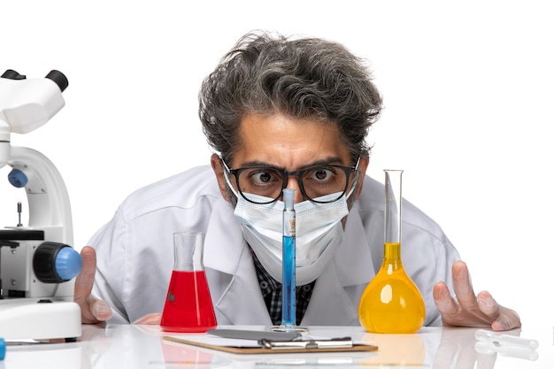 Front close view middle-aged scientist in special suit sitting with solutions and looking at them on white background male virus science covid chemistry