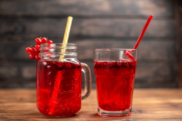 Front close view of natural organic fresh currant juice in a glass and a bottle served with tubes on a wooden table