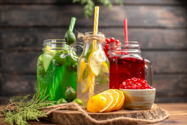 Front close view of organic fresh juices in bottles served with tubes and fruits on a wooden cutting board on a brown table