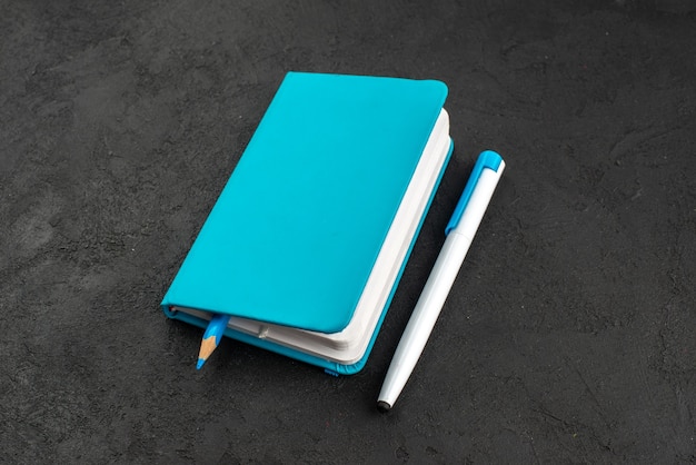 Вид спереди крупным планом ручки внутри закрытой синей записной книжки и ручки на черном