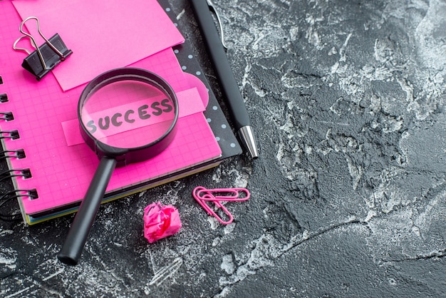 front close view pink notepad with pen magnifier and success note on gray background