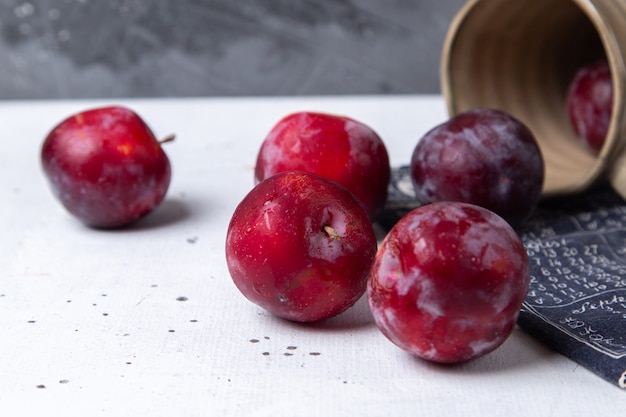 Free photo front close view red sour plums fresh and ripe all over the white desk