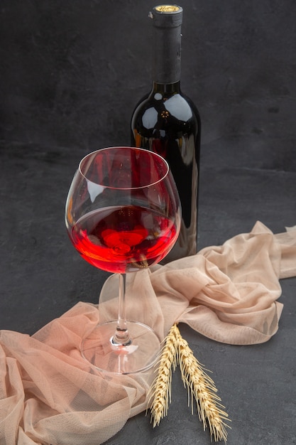 Vista frontale ravvicinata del vino rosso in un calice di vetro su un asciugamano e bottiglia su sfondo nero black