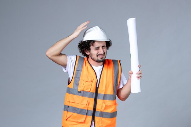 Front close view of scared construction worker in warning vest with safety helmet and holding blank on gray wall