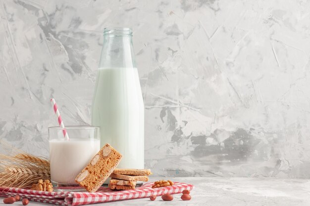 Front close view of stick shaped candy in glass cup bottle filled with milk and pastries peanuts on red stripped towel on the right side on gray background