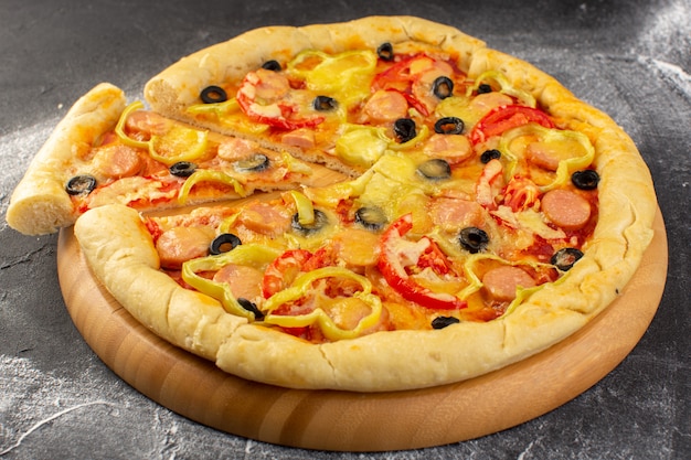 Front close view tasty cheesy pizza with red tomatoes, black olives, bell peppers and sausages on the dark surface