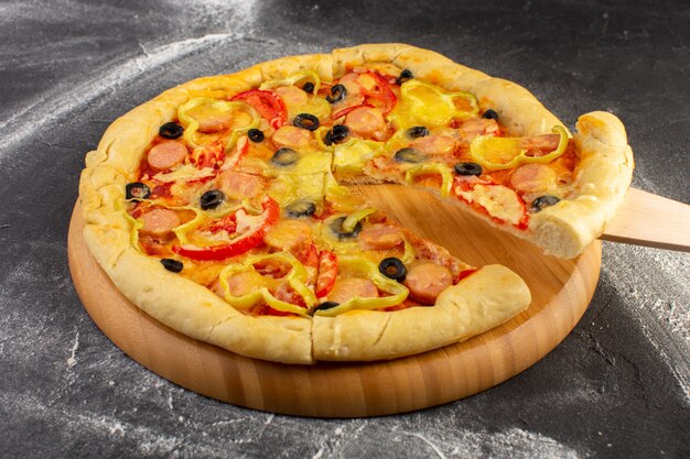 暗い表面に赤いトマト、ブラックオリーブ、ピーマン、ソーセージが付いている正面のおいしいチーズのピザ