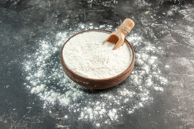 Front close view of white flour with wooden spoon inside and outside of brown bowl on gray background