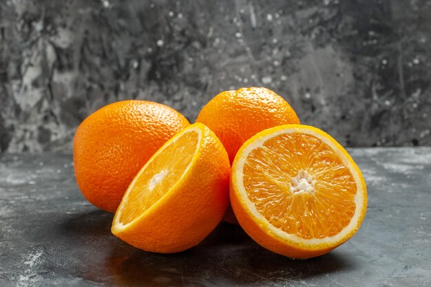 Front close view of whole and cut natural organic fresh oranges lined up in two rows on dark background