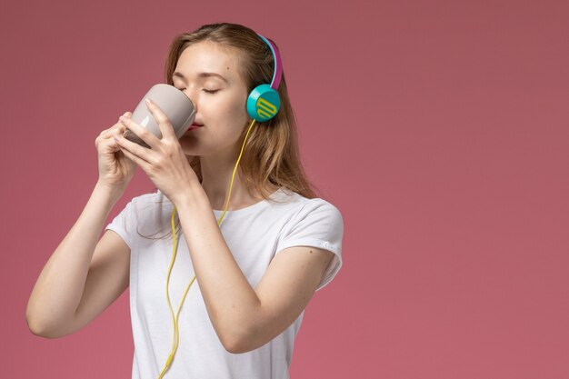 Front close view young attractive female listening to music and drinking tea on the pink wall model color female young