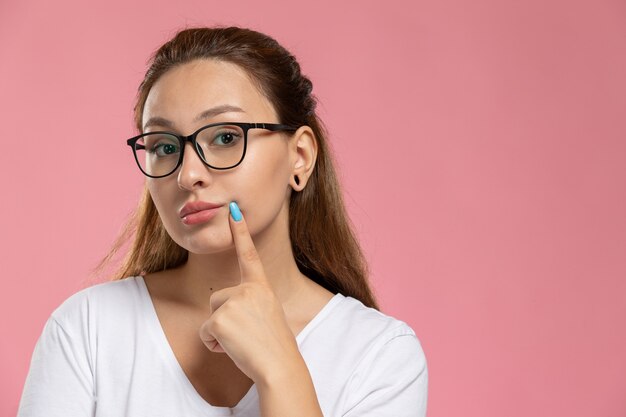 Front close view young attractive female in white t-shirt posing and thinking on the pink background