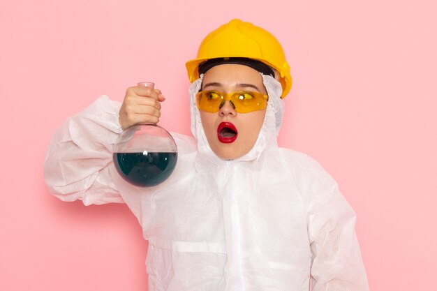 Front close view young beautiful female in special white suit wearing protective helmet holding solution on pink