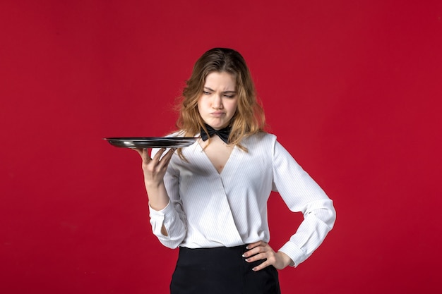 Front close view of young concerned female server butterfly on the neck and holding tray on red background