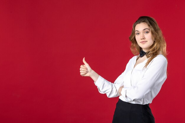 Front close view of young confident waitress girl butterfly on the neck and making ok gesture on the right side on red background