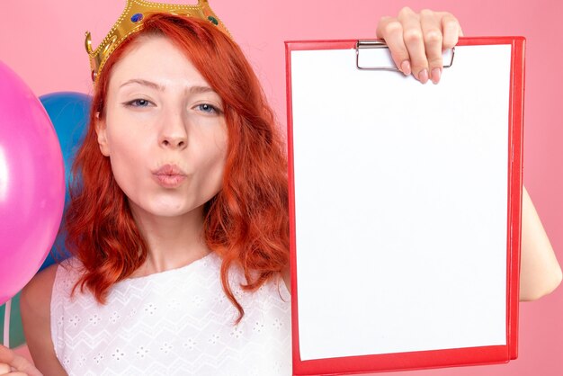 Front close view young female holding colorful balloons and file note on a pink 