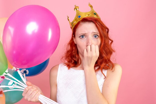 Front close view young female holding colorful balloons nervous on pink 