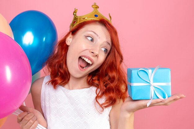 Front close view young female holding colorful balloons and present on a pink 