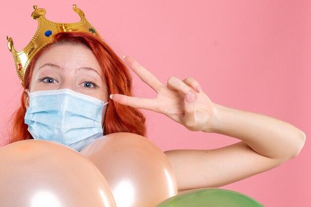 Front close view young female holding colorful balloons in sterile mask on pink 