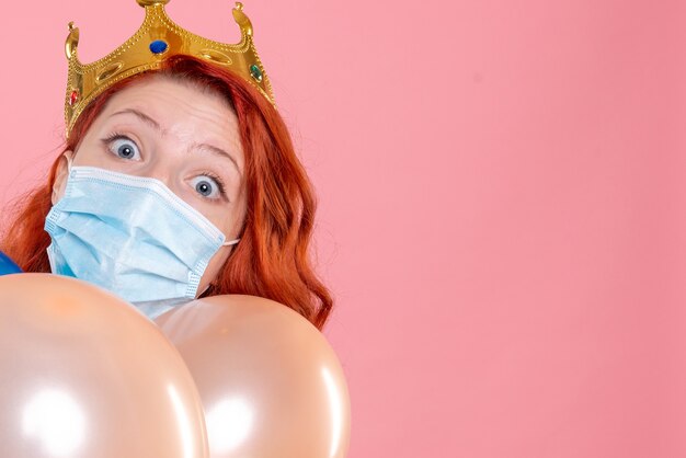Front close view young female holding colorful balloons in sterile mask on the pink 