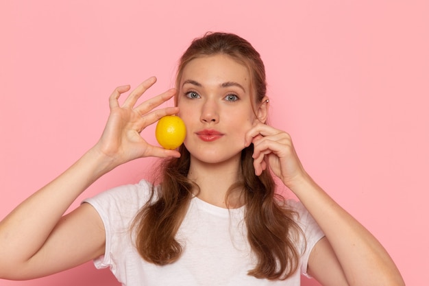 Front close view young female in white t-shirt holding fresh lemon on pink wall