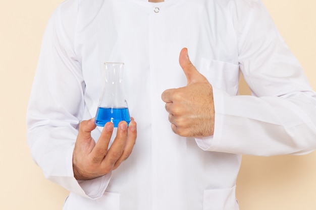 Free photo front close view young male chemist in white special suit holding a little flask with blue solution on cream wall science experiment chemistry scientific