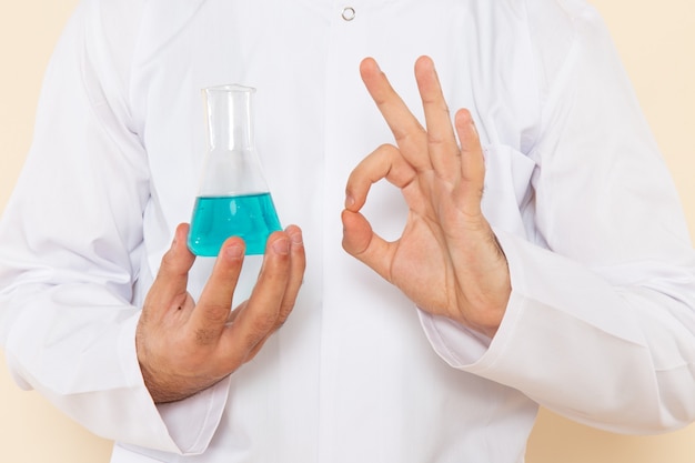 Front close view young male chemist in white special suit holding little flask with solution on light wall science experiment chemistry scientific