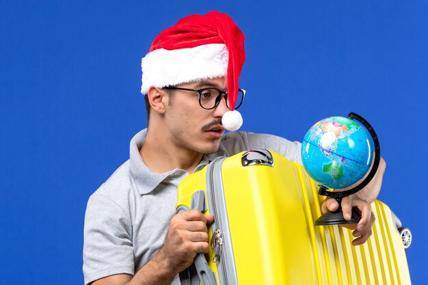 Front close view young male holding globe and yellow bag on blue wall plane vacation trip