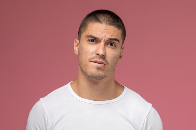 Front close view young male in white t-shirt posing with confused expression on pink desk