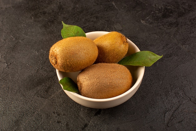 Foto gratuita un fronte chiuso chiuso kiwi marroni freschi maturi isolati succosi frutti morbidi e interi insieme con foglie verdi all'interno del piatto bianco