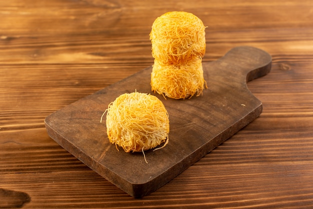 Free photo a front closed up view round sweet cakes delicious tasty cakes isolated lined on the brown wooden rustic desk