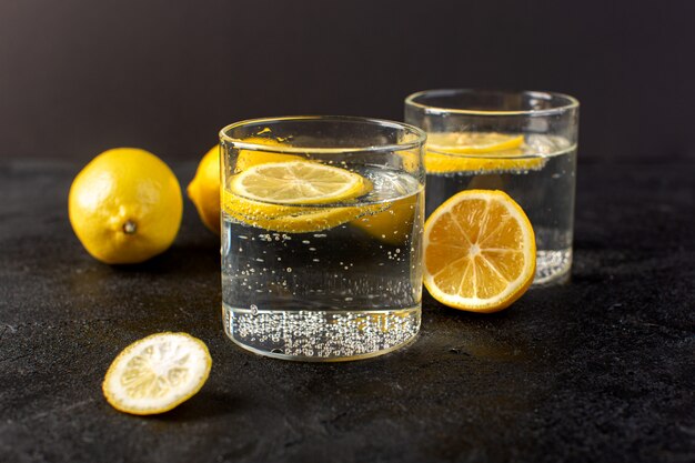 A front closed up view water with lemon fresh cool drink with sliced lemons inside transparent glasses