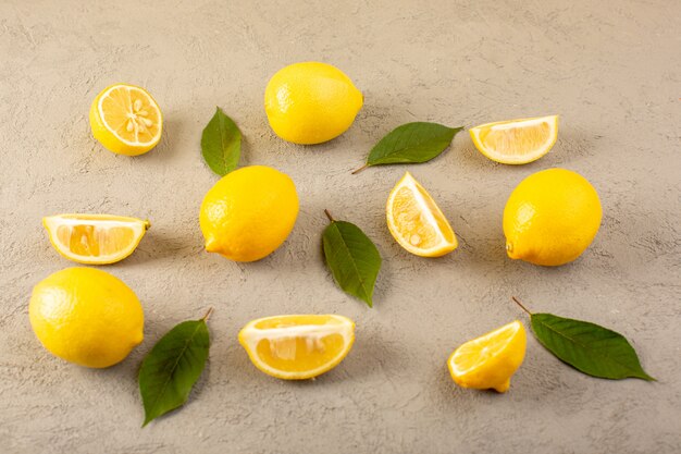 A front closed up view yellow fresh lemons ripe mellow and juicy whole and sliced with green leaves lined on the grey