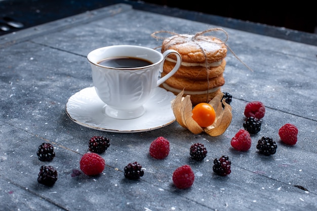 Front closer view cup of coffee with different berries and sandwich cookies on grey desk