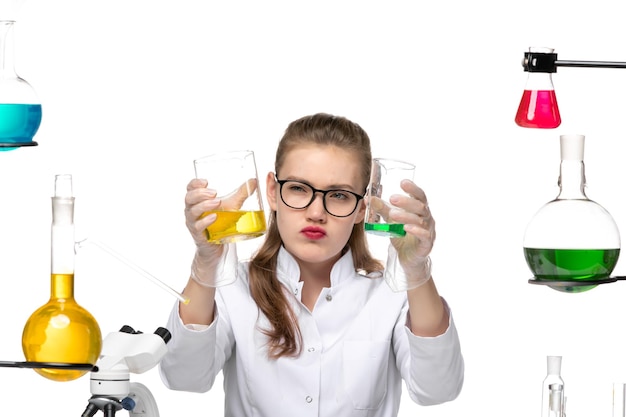 Front closer view female chemist in medical suit holding flasks with solutions on white background chemistry pandemic health covid