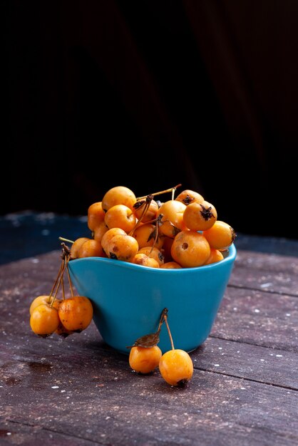 Front distant view yellow cherries mellow fresh and ripe inside blue bowl on brown wood