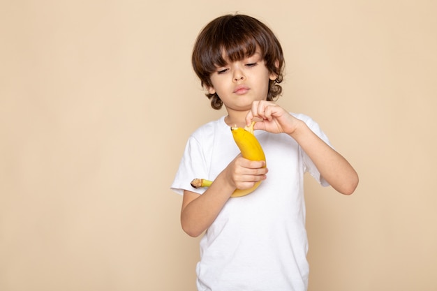 front portrait view, little cute boy adorable in white t-shirt with bananon pink wall