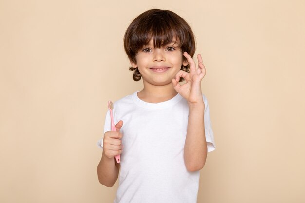 front portrait view, smiling boy cute adorable with toothbrush on pink wall