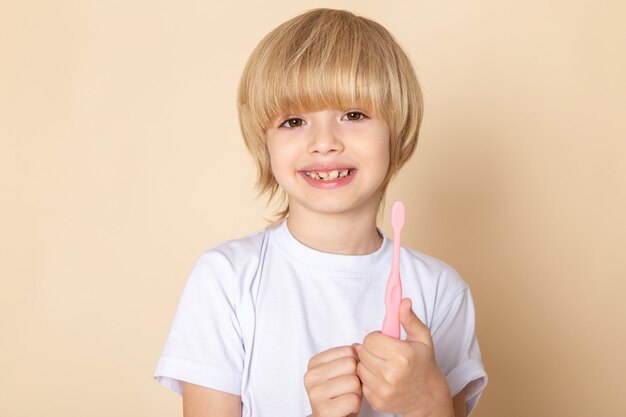 フロントポートレートビュー、ピンクの壁に白いtシャツで愛らしい小さなかわいい男の子の笑顔