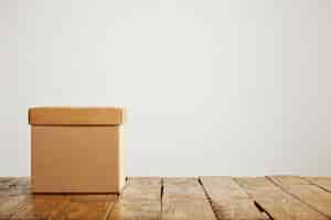 Бесплатное фото Фронтальный снимок квадратной бежевой картонной коробки без надписи с крышкой на деревянном полу, изолированной на белом