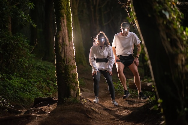 밤에 숲을 걷는 활동적인 남녀의 전면 모습. 낚시를 좋아하는 옷을 입은 두 명의 스포티한 사람들이 야외에서 시간을 보내고 있습니다. 레저, 자연, 취미 개념