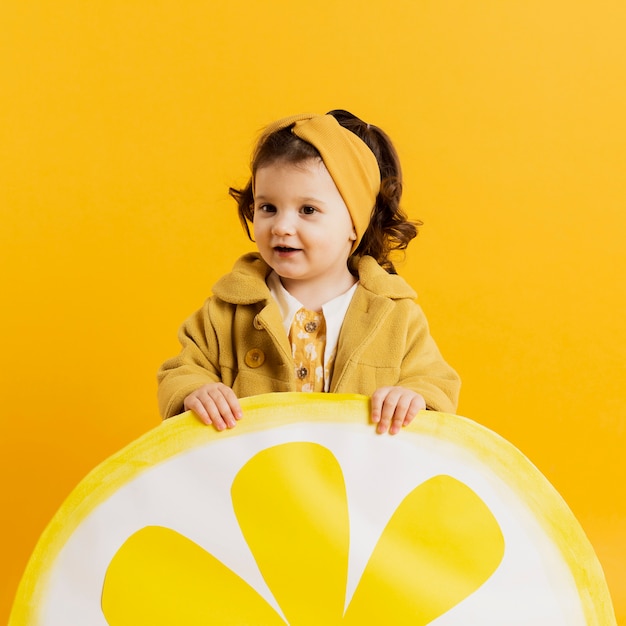 Vista frontale del bambino adorabile che posa con la decorazione della fetta del limone