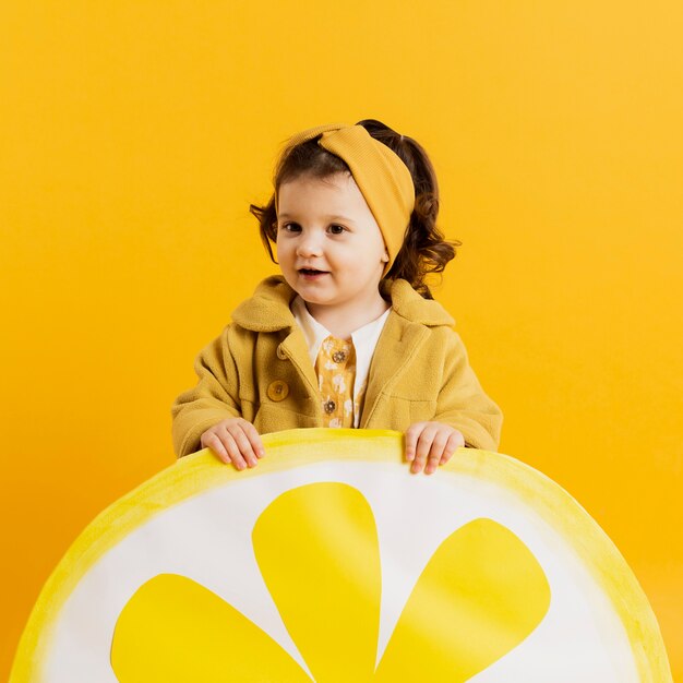 Вид спереди очаровательны ребенка позирует с украшением ломтик лимона